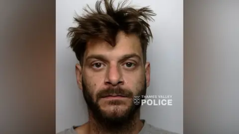 Thames Valley Police Custody photo of a man with messy dark brown hair and a beard