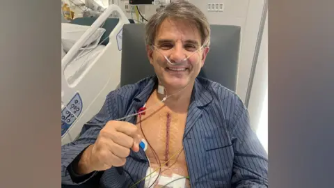 Supplied Jeremy Schwartz pictured following his heart surgery. He is clenching his right first and smiling to camera. Jeremy has a sizable scar on his chest and is wearing blue pyjamas.