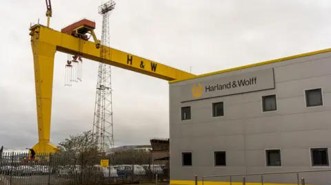 Getty Images One of the iconic Harland & Wolff Samson and Goliath yellow gantry cranes near the entrance to the Harland & Wolff shipyard building. The shy is cloudy. 