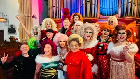 Drag queens stand in front of a church organ.