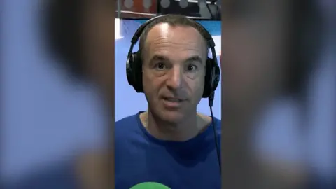 Martin Lewis looking at the camera, wearing headphones and a blue top