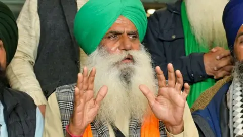 Farmer leader Jagjit Singh Dallewal, with a long, white bread and wearing a green turban, addressing journalists, who are not in the frame.