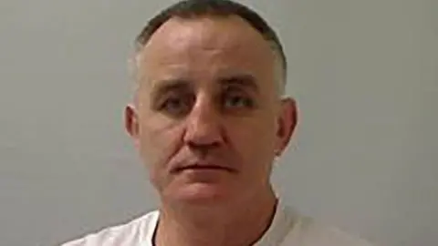 PA Media James Meehan is seen in a police stock photo wearing a white shirt. He has grey and black hair.