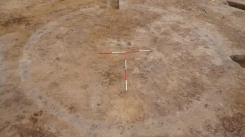 OCA A circular barrow revealed in sandy soil. Surrounding it are post holes. 