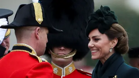 Princess of Wales, wearing a green head piece, smiles at a soldier wearing red uniform