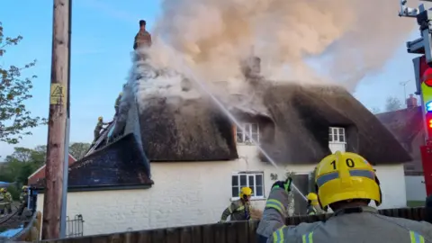 Dorset and Wiltshire Fire and Rescue Service Firefighters tackling a fire at a thatched roof property