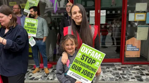 Unite Protesters in a street. A woman has her arm around a young girl who holds up a placard.