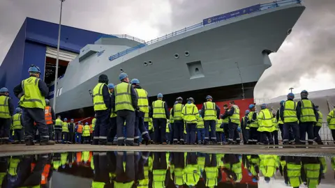 Getty Images HMS Venturer rolling off the assembly line with crowds of workers in high visibility vests watching on.