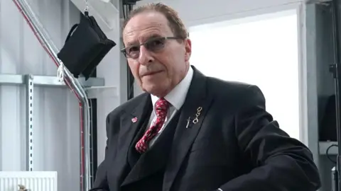 Peter James in a dark suit and red tie.