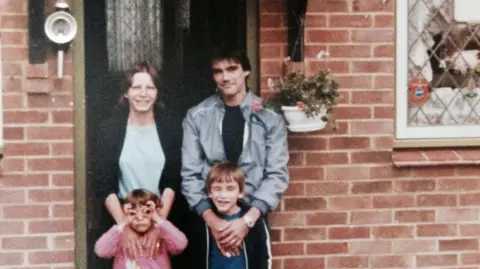 Matt Lane An old colour photo of a family of four stood in front of a red-brick house.
