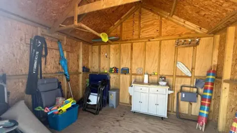 Elvins Estate Agents Inside of the wooden beach hut shows a large open-plan space with various different beach items including chairs, wind shield and toys. 