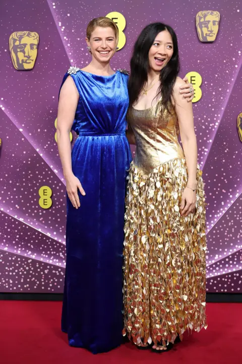 Getty Images Jessie Buckley in a long blue dress and Chloé Zhao in a gold dress