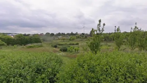 Google Former allotments, now slightly overgrown, with housing and a wind turbine visible in the background