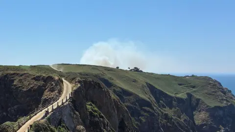 BBC A picture of Little Sark - there is a large white plume of smoke.