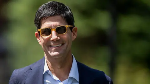 Getty Images Federal Reserve chairman Kevin Warsh is pictured smiling in yellow sunglasses with a navy suit jacket and white shirt. 