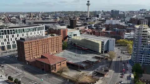 A drone shot of Canning Place, in Liverpool city centre. It is a large brown building with an empty car park, surrounded by numerous buildings.