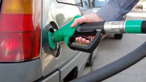 A man fills a grey car with petrol using a pump.