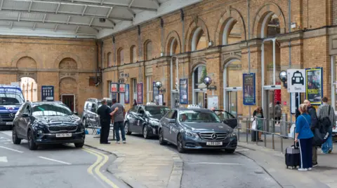 Taxis on a rank outside York railway station with people queuing