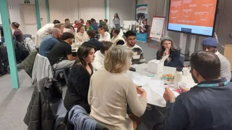 A group of people sitting down at a meeting between leaders and refugees.