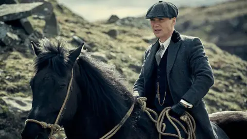 BBC / Caryn Mandabach Productions Ltd / Robert Vigilasky Cillian Murphy is wearing a flat cap and three-piece suit while riding a horse in a scene from Peaky Blinders.