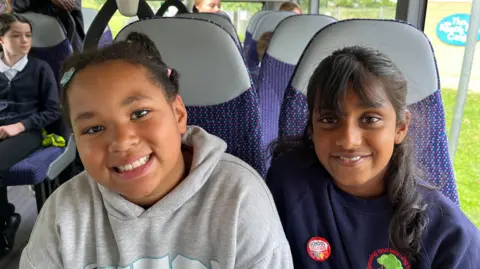 Two girls smile at the camera as they ride on the bus as part of a promotional event for Kids Go Free.