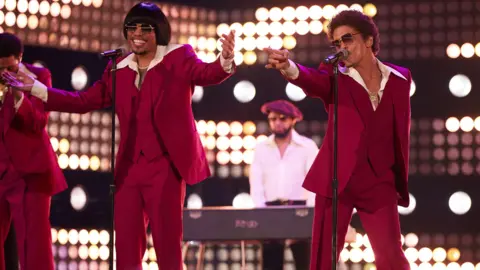 Getty Images Anderson .Paak and Bruno Mars of Silk Sonic perform onstage during the 2022 Billboard Music Awards in matching burgundy suits and cream shirts, with sunglasses on.