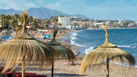 Getty Images A general view of the beach in Mijas, Spain. It is busy with people who are walking, swimming or sunbathing. There are lots of umbrellas spread along the sand.