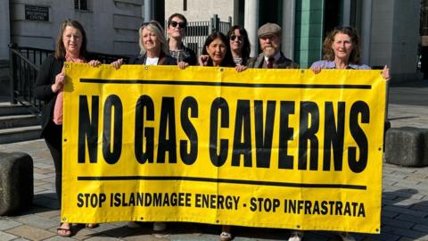 People outside a court building holding a yellow sign with black writing that says no gas caverns 