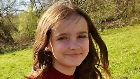 Family handout Aria Thorpe pictured outside. She has long dark hair and brown eyes. She is squinting in the sun and smiling. Grass and trees can be seen behind her.