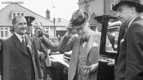 Winston Churchill getting out of a car, surrounded by his bodyguards
