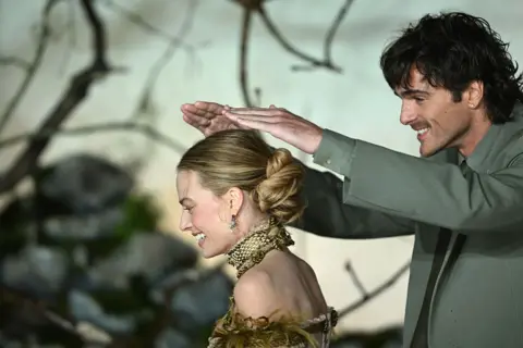 WireImage/GettyImages Jacob Elordi puts his hands above Margot Robbie's head in an attempt to shield her from the rain as they both smile.