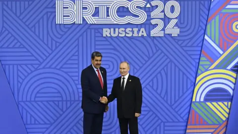 Getty Images Venezuelan President Nicolás Maduro shakes hands with his Russian counterpart, Vladimir Putin, in front of a sign promoting the 2024 BRICS summit in Kazan.