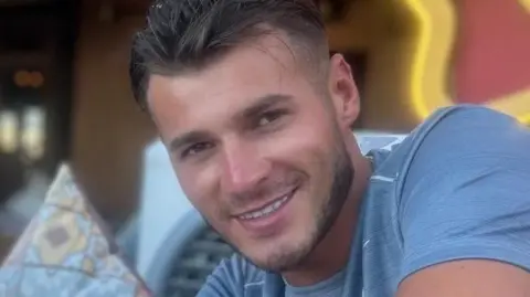 blue stevens, man in blue t-shirt smiling at the camera. He has short brown hair and slight stubble.