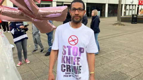 Shariqua Ahmed/BBC Uri, a man, wearing a white T-shirt with 'stop knife crime' message.