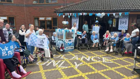 MHA Abbey Park Staff and residents wear Coventry City tops, with many holding flags. 