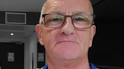 Headshot of Steven Richardson inside a building. He is wearing glasses and looking at the camera and has short grey hair. 