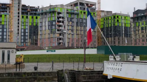 An apartment block covered in scaffolding and building materials. It is situated beside the SS Nomadic boat at the Titanic slipway. 