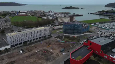 A drone shot of Millbay in Plymouth with several high-rise buildings in the foreground and the open sea in the background