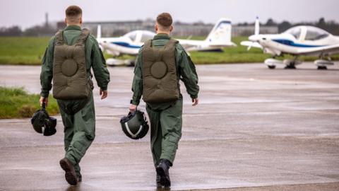 Two male pilots walk towards their planes