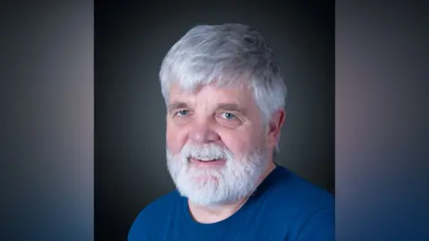 Robert Sergeant A headshot of an older man with a white beard and white hair. He is wearing a dark blue top. 