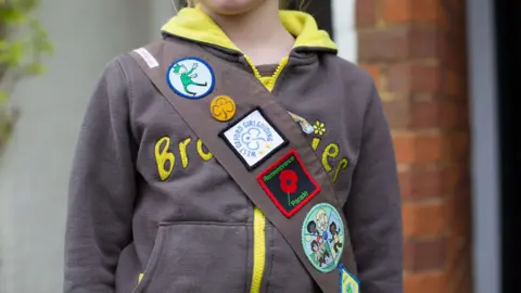 A girl wearing a Brownie hoodie and a sash with a badge 