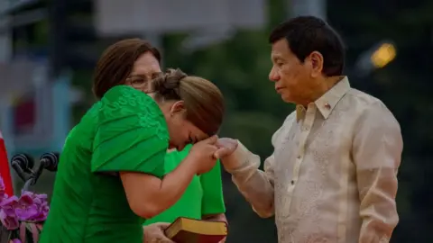 Getty Images Sara Duterte wearing a bright green dress kisses the hand of her father Rodrigo Duterte during her inauguration as vice president of the Philippines in Davao City in June 2022.