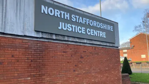 A large sign across the top of a red brick wall reads 'North Staffordshire Justice Centre.'