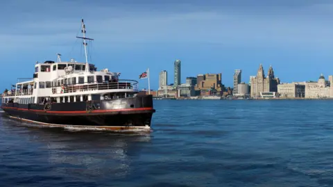 The Royal Iris of the Mersey as she sails near the Liverpool Waterfront with the Royal Liver building in the distance.
