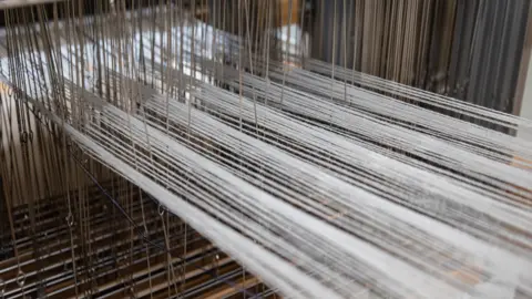 Tegen Kimbley A close-up image of yarn being threaded through a loom