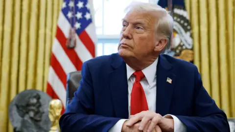 Getty Images Donald Trump in the Oval Office. He is wearing a blue suit with a US flag pin. 