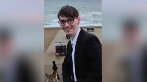 A young man in glasses and a suit on a beach