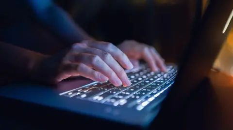 Close up of woman's hand typing on computer keyboard in the dark, working late on laptop at home