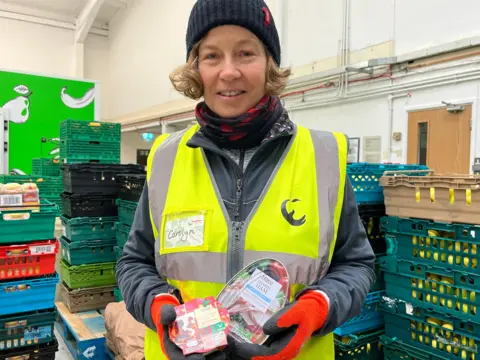 Julia Gregory/ BBC A volunteer holds donate Christmas food.