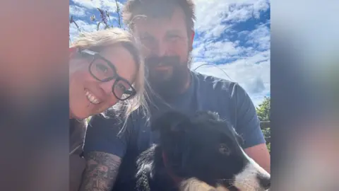 Ian Constable Ian Constable and his partner smiling for the camera with their dog on a sunny day.